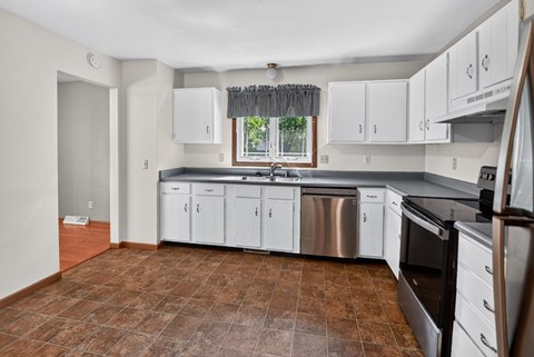 A kitchen with white cabinets and brown tiled floors.
