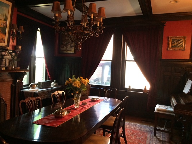 A dining room with a chandelier, a table with a vase of flowers, and a window with red curtains.