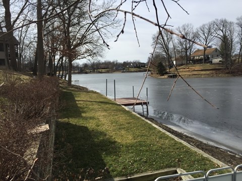 A lake surrounded by trees and a house in the distance.