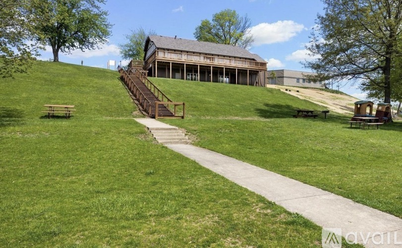 A large building with a staircase leading up to it is situated on a grassy hill.