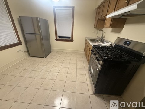 A kitchen with a black stove top oven, a silver refrigerator, and a window with blinds.