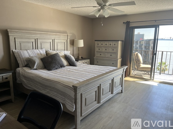A bedroom with a large bed, a dresser, and a balcony with a chair.