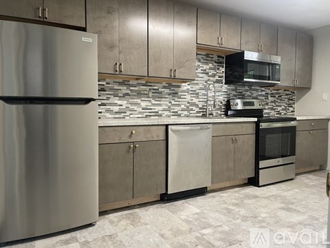 A kitchen with a stainless steel refrigerator and a stone backsplash.