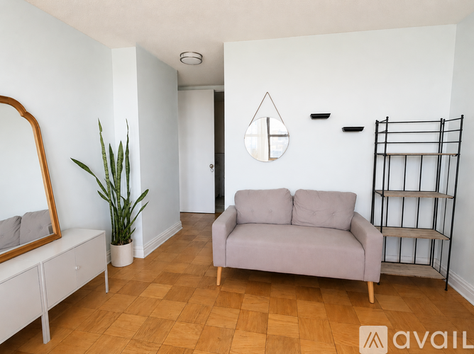 A living room with a grey couch, a wooden floor, and a mirror on the wall.