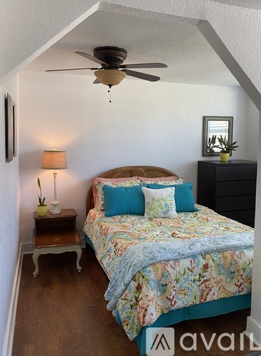 A bedroom with a bed, a ceiling fan, and a nightstand with a lamp.