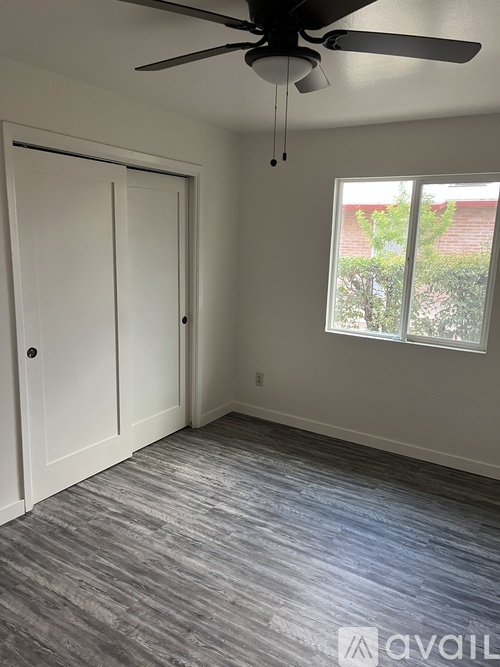 A room with a ceiling fan and a window with a view of a tree and a building outside.