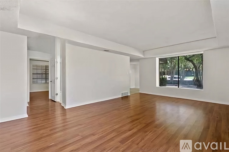 A room with wooden floors and white walls, with a window showing trees outside.