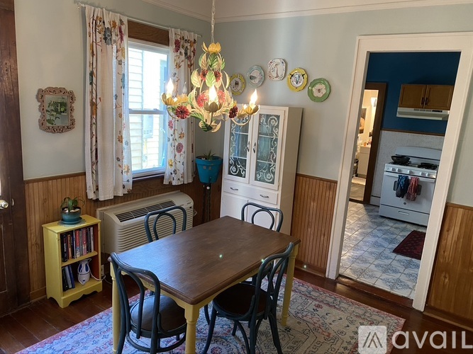 A dining room with a wooden table and chairs, a chandelier, and a bookshelf.