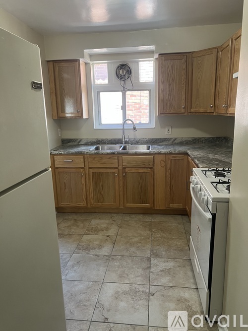 A kitchen with a white refrigerator, wooden cabinets, and a tiled floor.