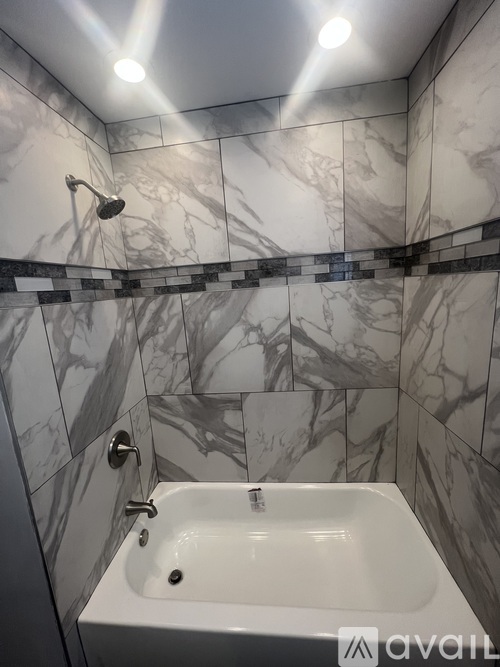 A bathroom with a marble tile wall and a white bathtub.
