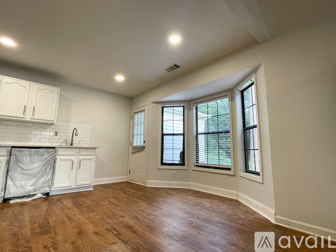 A room with wooden floors and white walls, with a window and a sink visible.
