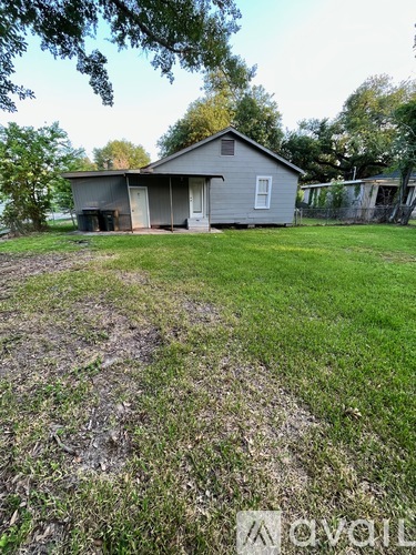 A house with a grey roof and a white door is surrounded by a grassy area.