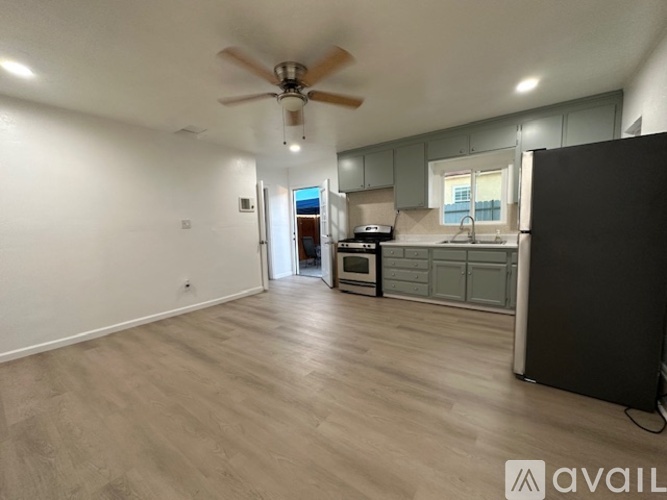 A spacious room with a ceiling fan and lighting, leading to a kitchen area with a microwave and oven.