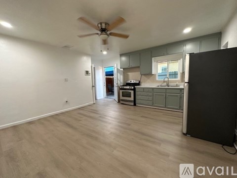 A spacious room with a ceiling fan and lighting, leading to a kitchen area with a microwave and oven.
