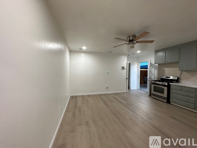 A room with a fan and a kitchen area in the background.