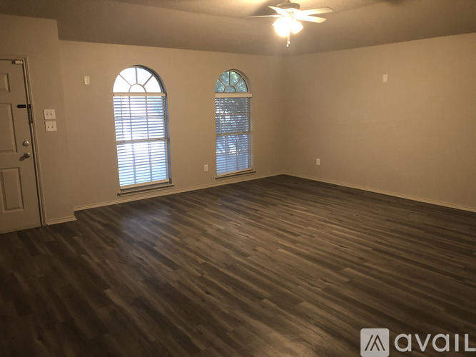 A room with wooden flooring and two windows.