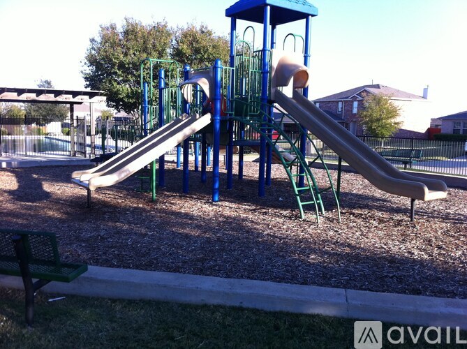 A playground with a blue and green slide and a green bench.