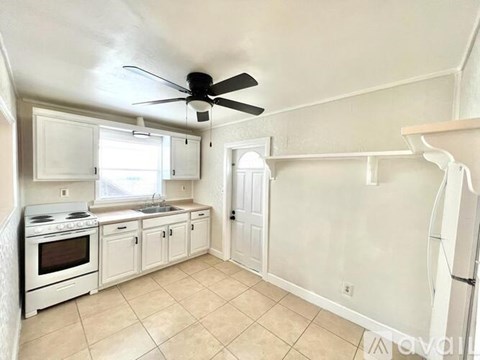 A kitchen with white cabinets and appliances, a ceiling fan, and a window.