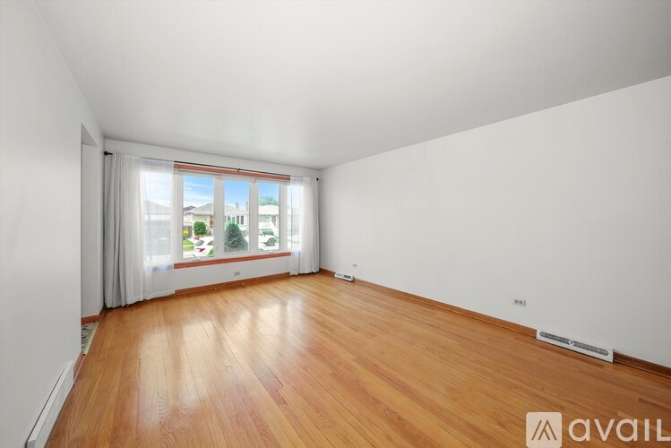 A room with wooden flooring and a window with a view of a tree and buildings outside.