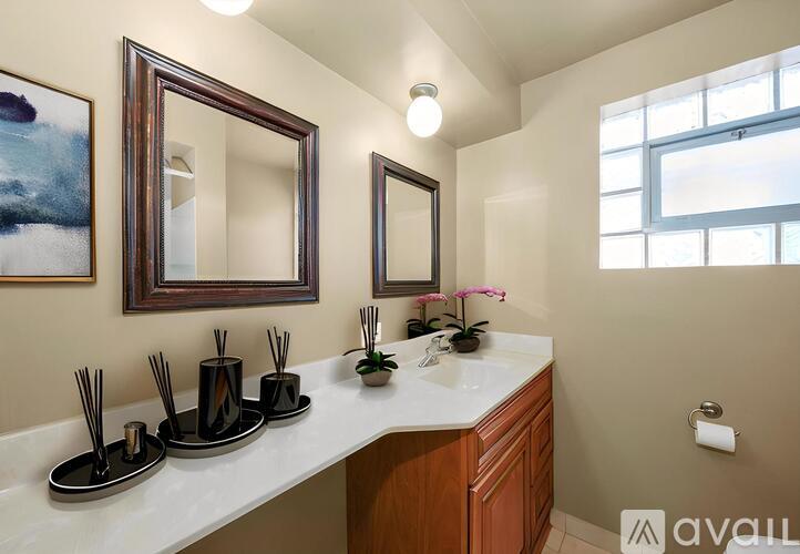 A bathroom with a vanity, two mirrors, and a painting on the wall.