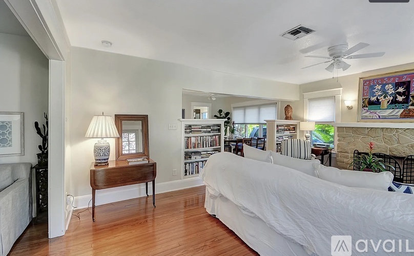 A bedroom with a white bed and a wooden table with a lamp on it.