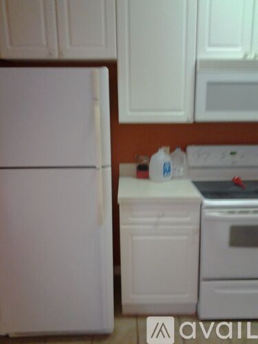 A white refrigerator is in a kitchen with white cabinets.