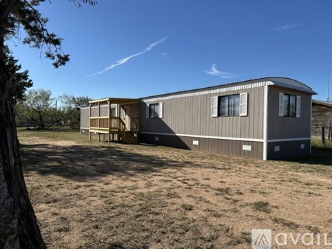 A mobile home sits in a grassy field with trees in the background.