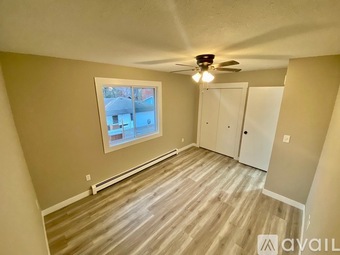 A room with a ceiling fan and a window overlooking a building.