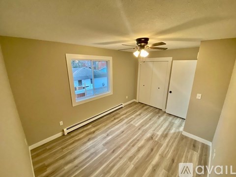 A room with a ceiling fan and a window overlooking a building.