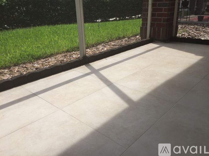 A patio with a tiled floor and a glass door leading to a grassy area.