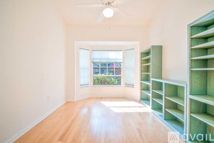A room with a ceiling fan and a large window with a view of a building.
