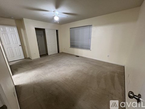 A room with a carpeted floor, a ceiling fan, and a door leading to another room.
