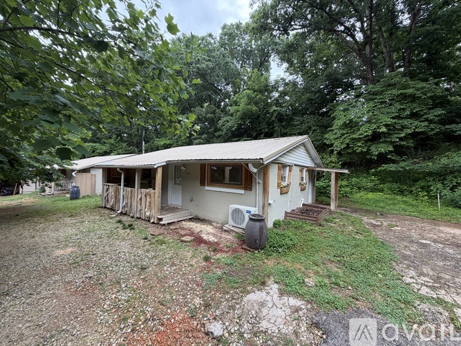 A house with a porch and a covered patio is surrounded by trees.
