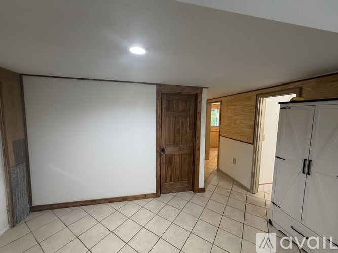 A room with a white ceiling, a wooden door, and a white floor with tiles.