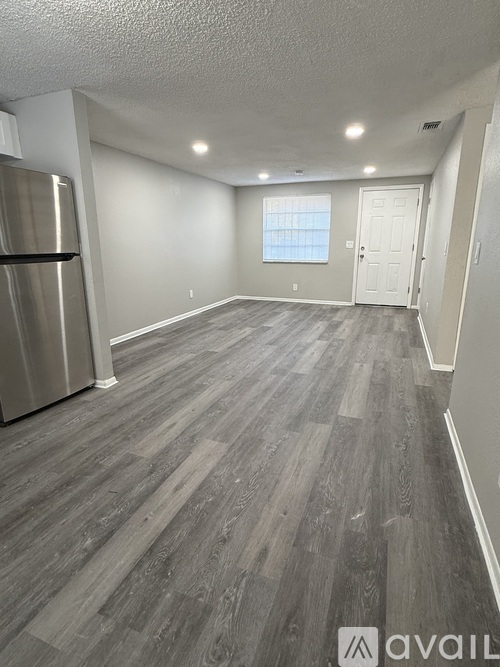 A spacious room with a wooden floor and a stainless steel refrigerator.