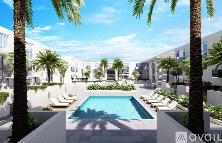 A pool surrounded by palm trees and lounge chairs in a sunny courtyard.