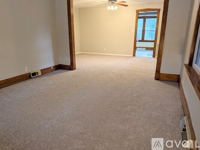 A room with a carpeted floor, a ceiling fan, and a door leading outside.