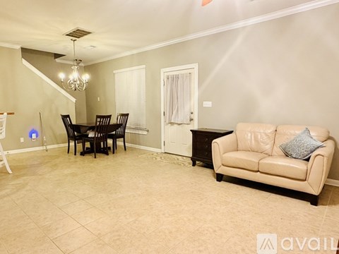 A living room with a beige couch, a dining table with chairs, and a chandelier.