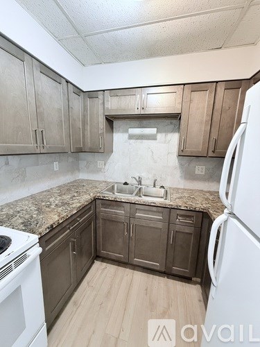 A kitchen with a white refrigerator, brown cabinets, and a marble countertop.