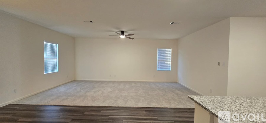 A spacious room with a ceiling fan and two windows.