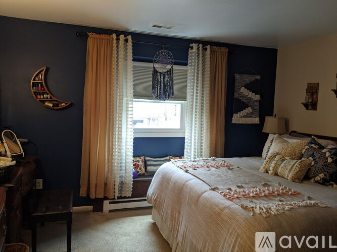 A bedroom with a bed, a window with curtains, and a dream catcher hanging from the window.