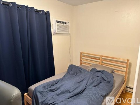 A bedroom with a bed, chair, and air conditioner.