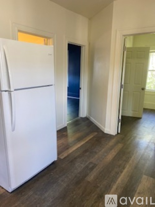A white fridge in a room with wood flooring and a door.