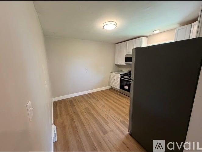 A kitchen area with a black refrigerator and wooden flooring.