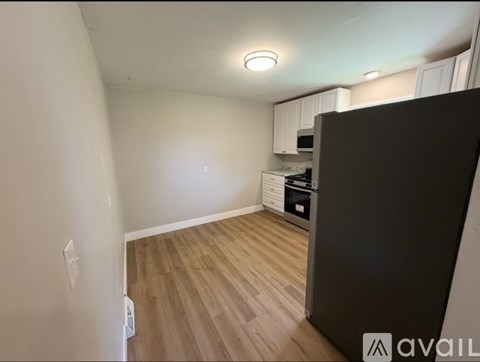 A kitchen area with a black refrigerator and wooden flooring.