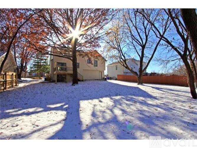 A house with a snow-covered yard and trees with orange leaves.