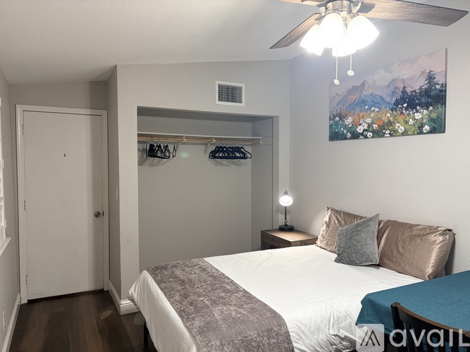 A bedroom with a bed, a ceiling fan, and a painting on the wall.