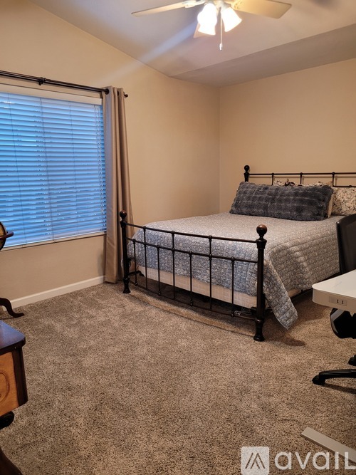 A bedroom with a bed, a window with blinds, a ceiling fan, and a carpeted floor.