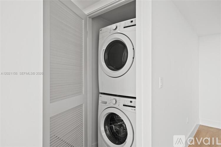 A white washing machine is stacked on top of another in a small, white-walled laundry room.