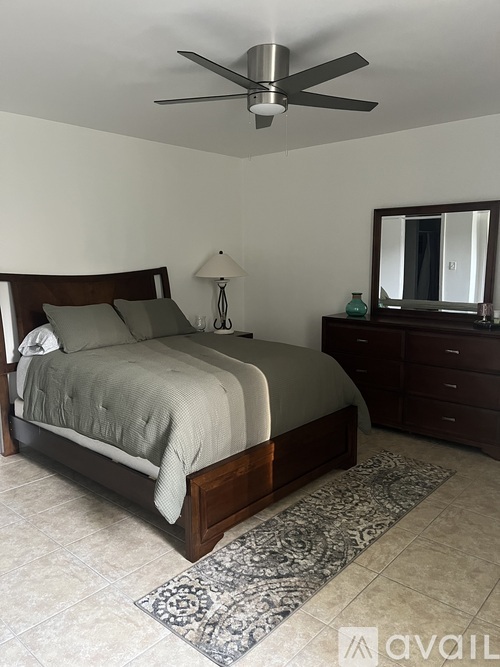 A bedroom with a bed, dresser, mirror, and rug.